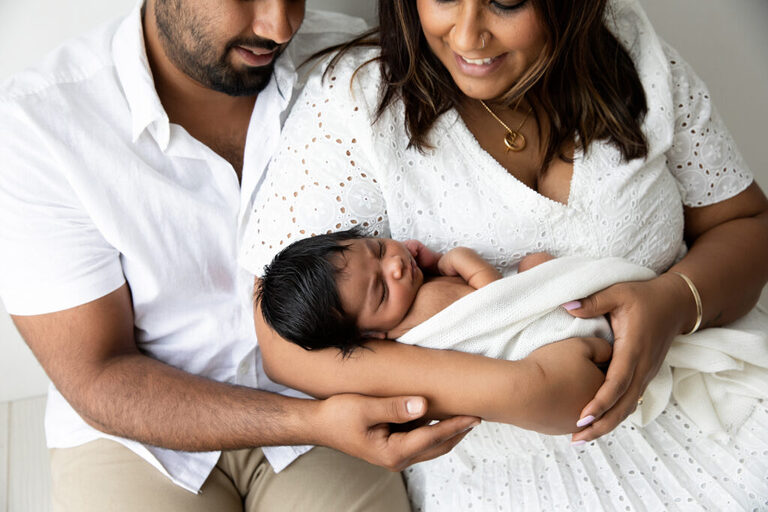 Family photographers parents with newborn baby in arms smiling 